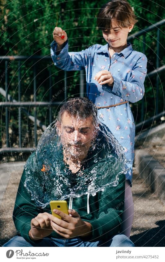 Girl blowing up a water-filled balloon over her father's head burst splash daughter wet pop spray action impact background explosion motion speed dew shot drop