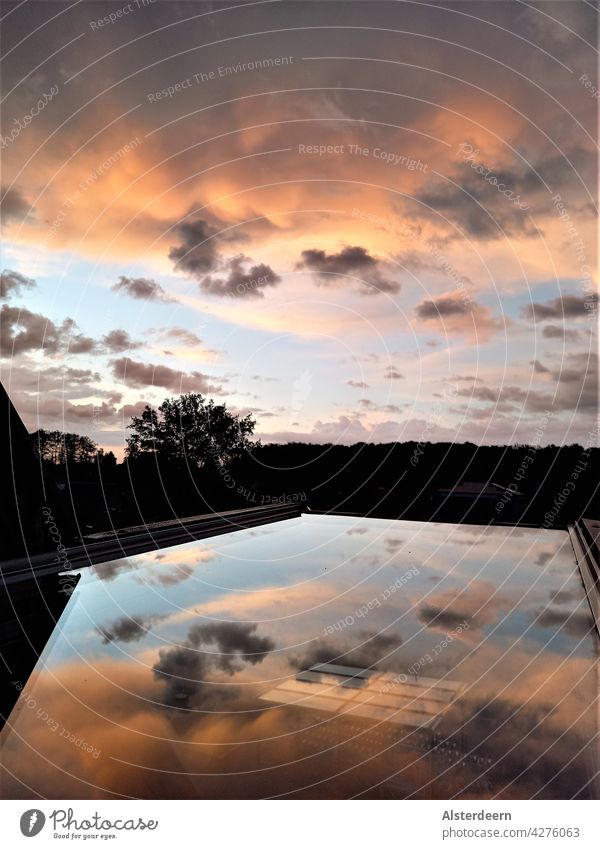 Setting sun from a wide open skylight in which the compact clouds illuminated by the sun are reflected in between scattered clouds with a view of the horizon.