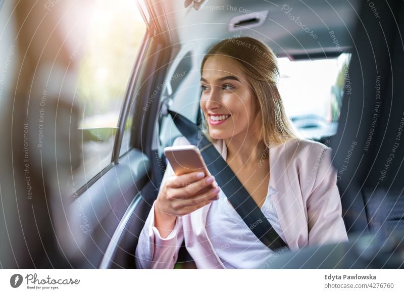 Young woman with smartphone on the back seat of a car carsharing confident smiling satisfaction female attractive beautiful young adult joy positive content