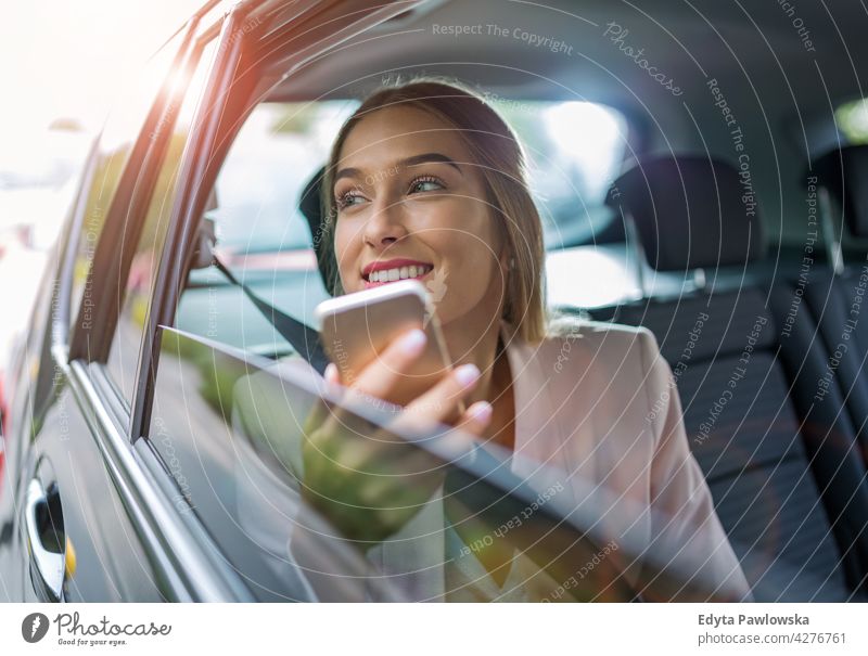 Young woman with smartphone on the back seat of a car carsharing confident smiling satisfaction female attractive beautiful young adult joy positive content