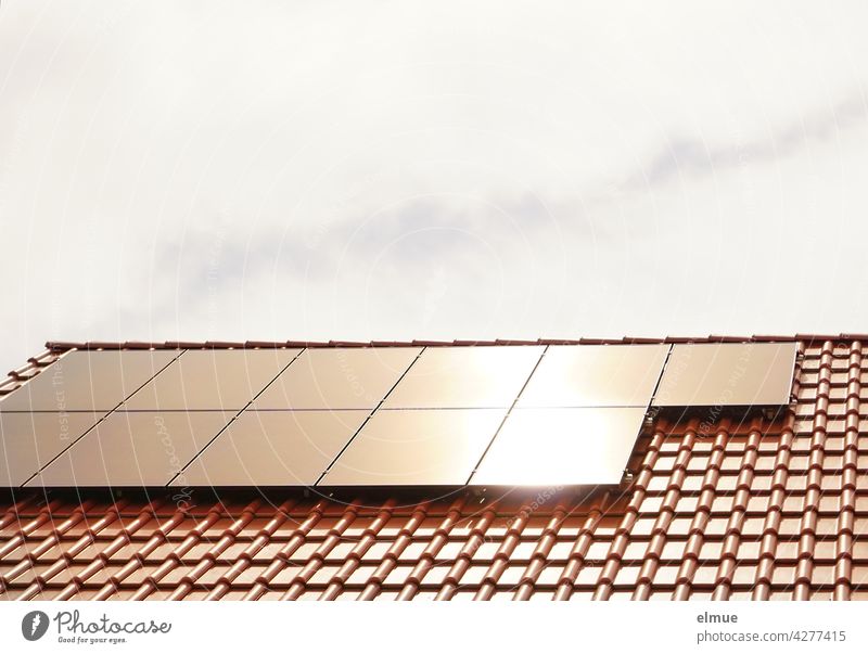 The sun is reflected in the eleven solar collectors on the red tiled roof of a residential building / Power generation / Green electricity / Photovoltaic system