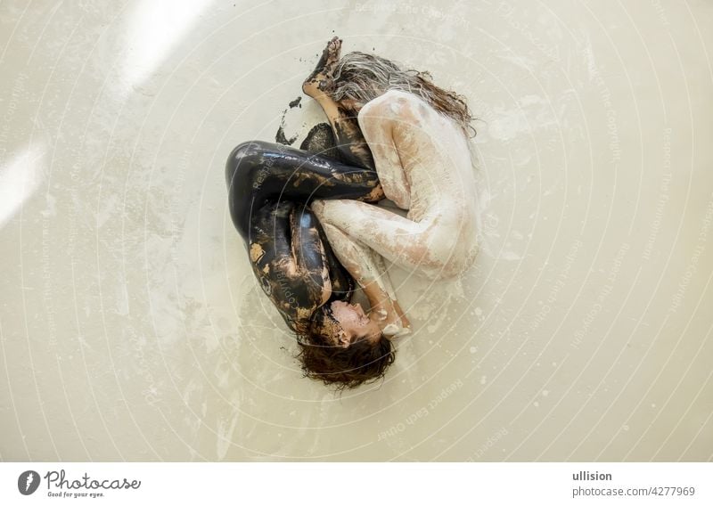 Two artistically abstract painted young sexy women, girlfriends in black and white color lying like a Yin Yang symbol on the floor in the studio, copy space.