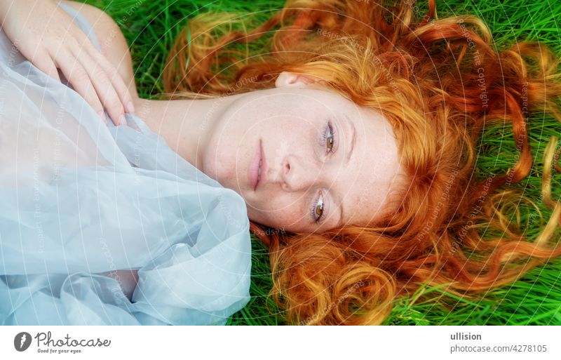 Portrait of a beautiful young sexy red-haired woman, lying in the spring sun in happiness, relaxing on the grass, the red hair draped freely around the head.