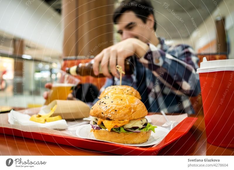 man eating fast food burger and drinking beer alone in the open area of a restaurant in a shopping mall meal bar happy pub male people lunch dinner hamburger