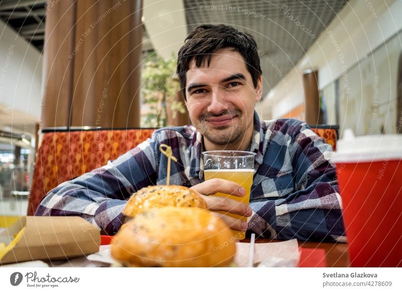 man eating fast food burger and drinking beer alone in the open area of a restaurant in a shopping mall meal bar happy pub male people lunch dinner hamburger