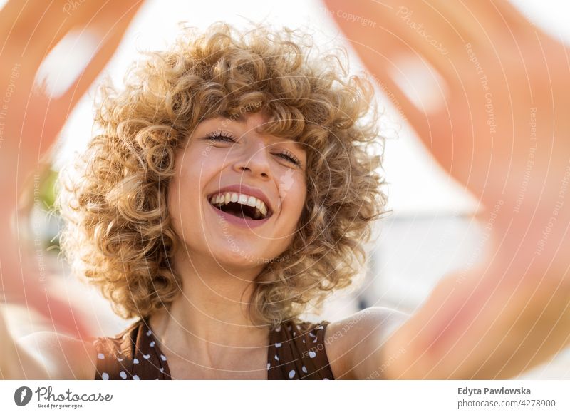 Portrait of young woman with curly hair smiling millennials urban street city stylish people young adult casual attractive female happy Caucasian toothy