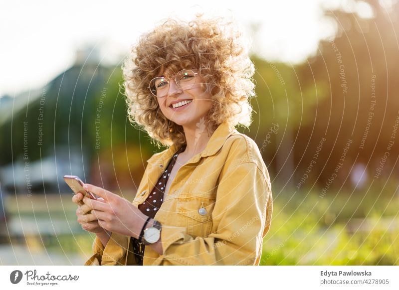 Young woman with mobile phone in the city millennials urban street stylish people young adult casual attractive female smiling happy Caucasian toothy enjoying