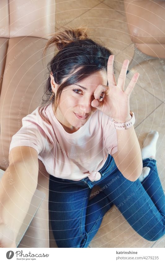 Young women sitting on the floor and taking selfie while showing OK finger sign ok gestures signm smile wear mockup t-shirt top view hand Lifestyle jeans indoor