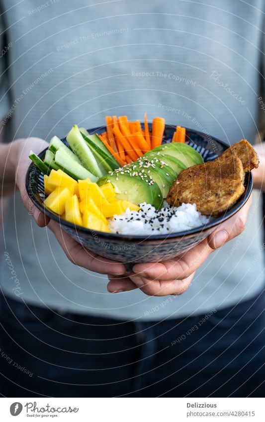 A female in a green shirt holding a fresh poke bowl with mango, avocado and tofu, vegan bowl, vertical asian background chopsticks copy space cucumber cuisine