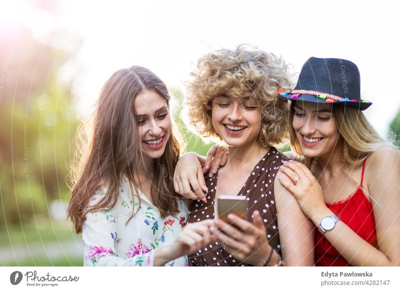 Happy young women having fun with smart phone sunset summer group together people woman casual beautiful attractive girl girls female three people friends