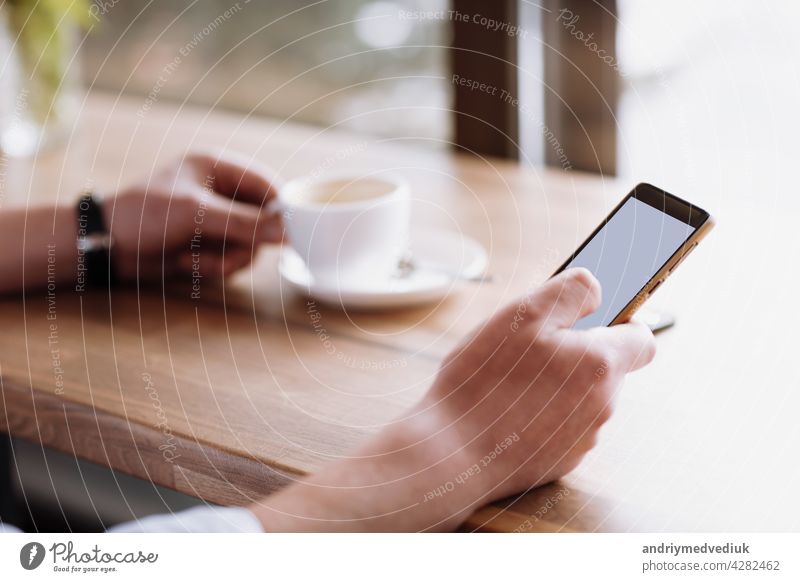 businessman hand holding a phone with isolated screen against moke up and drink coffee in the coffee shop blurred coffee cup background, Mock up concept