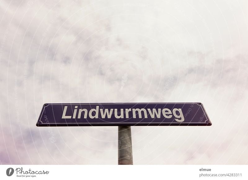 purple street name sign with white writing " Lindwurmweg " in front of cloudy sky / orientation street sign Street sign lindworm unusual street names dragon