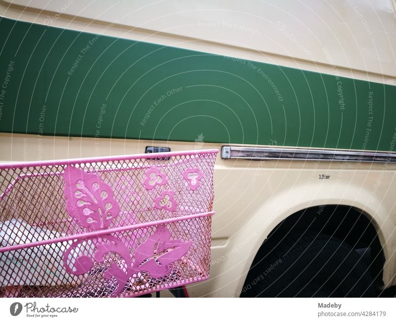 Old camper in beige with green stripe and bicycle basket in pink with floral pattern in the summer in the Hanseatic city of Hamburg Bicycle Wheel Basket Pink