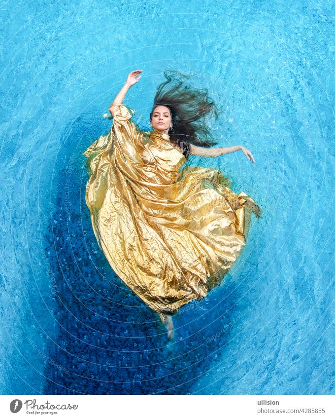 Top view of a beautiful young sexy woman in golden dress, evening dress, towel floats weightlessly elegantly swimming in the pool water cloth mermaid blue