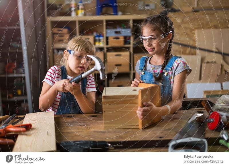 Two little girls building birdhouse in garage workshop working people child children kid kids girl power Skill craft Garage Hobby Lifestyle tools Concentration