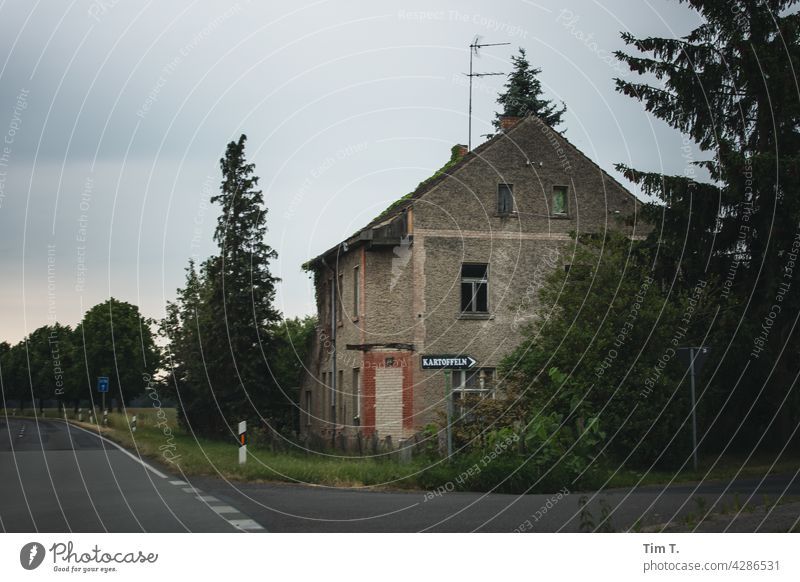 an old house on a Brandenburg country road . A sign in front of it with the inscription potatoes shows the way. Potatoes Country road Street Tree Deserted