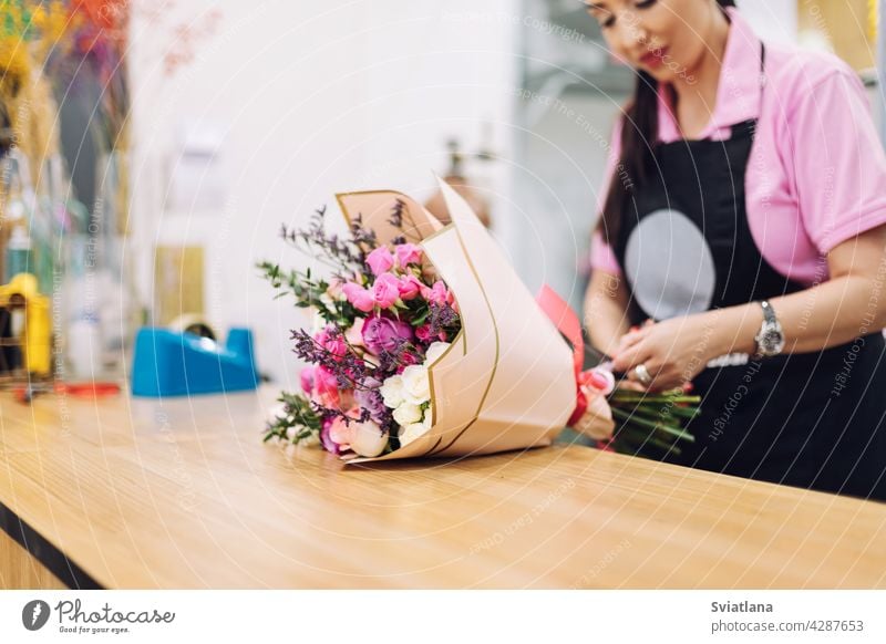 Close-up of a beautiful bouquet of flowers a florist girl is wrapping in gift paper. Flower business, working with flowers, flower bouquet packaging female