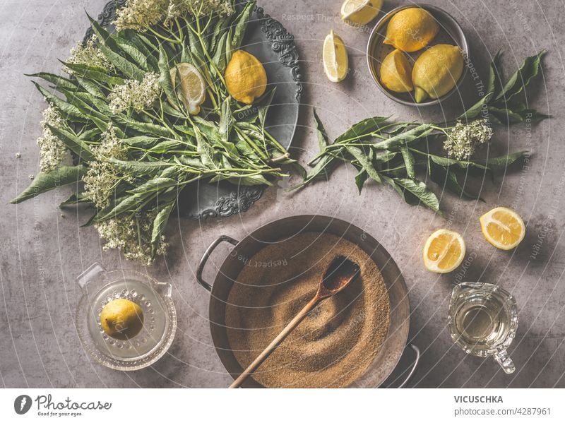 Kitchen preparation with fresh elder, lemon juice and sugar, bowl with spoon. Summer theme, dark concrete background. Top view kitchen summer top view