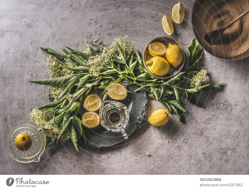 Homemade elder flower syrup with lemons, sugar, fresh lemon juice. Bundle of elder on decorated plate, kitchen equipment, dark concrete background. Top view