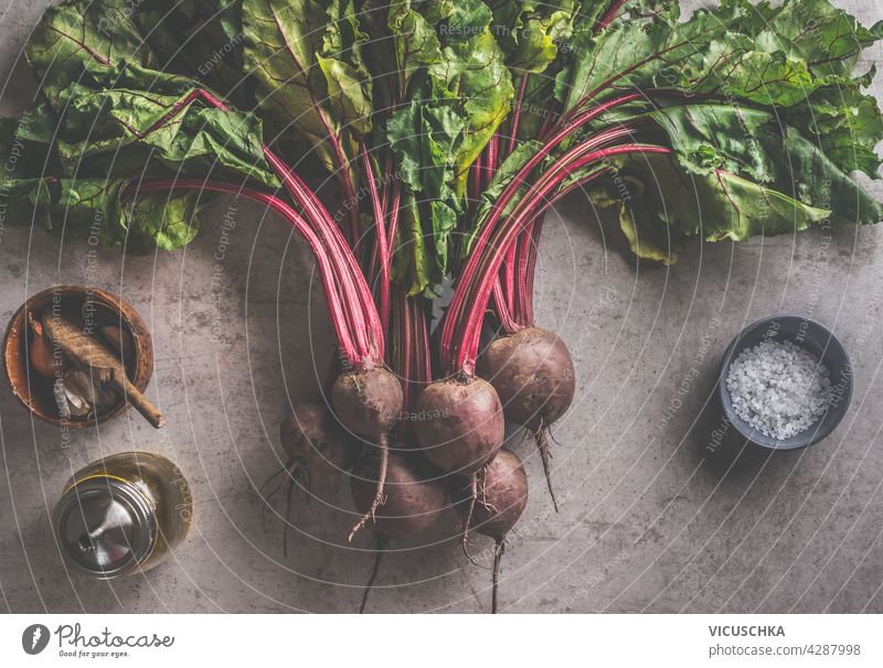 Fresh bundle of beetroot with greens leaves and cooking ingredients: olives oil, salt and garlic on dark concrete background.  organic vegetables. Healthy food concept. Top view