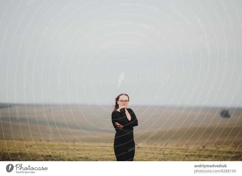 Young girl 20-25 years old in glasses and a black dress posing on a field background woman young outdoor beauty fashionable pose nature model romantic portrait