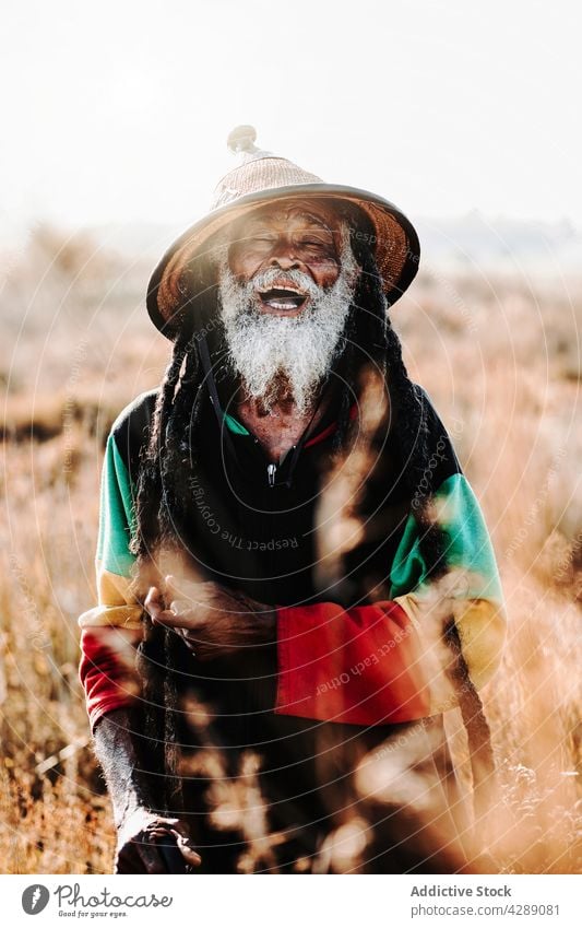 Happy hippie rastaman standing on field rastafarian happy smile male delight cheerful culture ethnic reggae caribbean nature african american native meadow hat