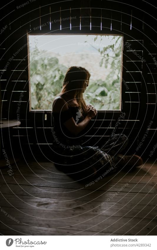 Serene woman sitting in wooden shack cabin window tropical plant tree countryside hut thailand tranquil exotic peaceful rest green female serene summer flora