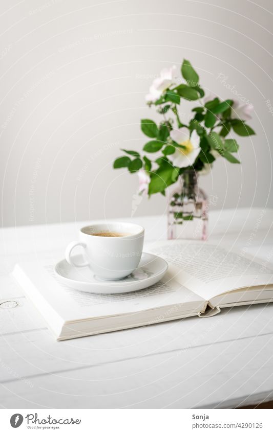 A cup of coffee on an open book and flowers in a vase on a white wooden table Coffee Cup Bay Open Wooden table White Vase Still Life at home Coffee break