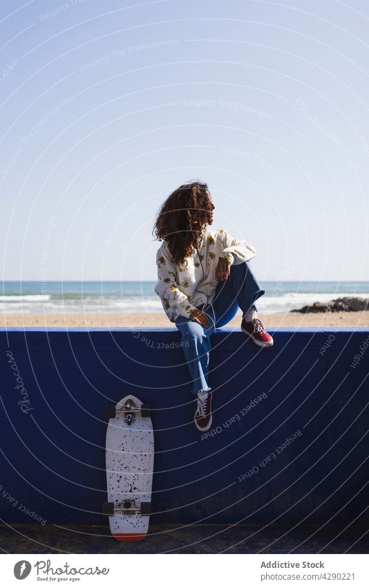 Woman sitting on railing against seafront woman skateboard handrail seaside seashore hobby coast sporty skateboarder thoughtful waterfront sand female positive