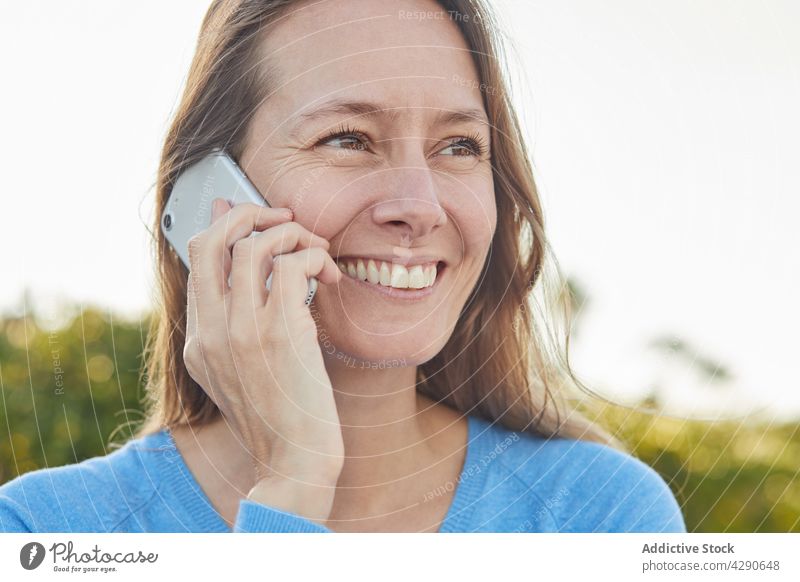 Lady having phone call near shrubs in street woman cellphone smile bush city garden female adult modern plant aged toothy smile exterior historic town lady