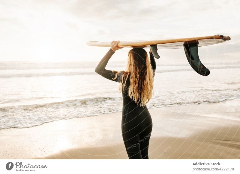 Anonymous female surfer standing at the beach with surfboard woman nature sunset wave outdoors wetsuit seacoast sportswoman surfing hobby ocean seaside carrying