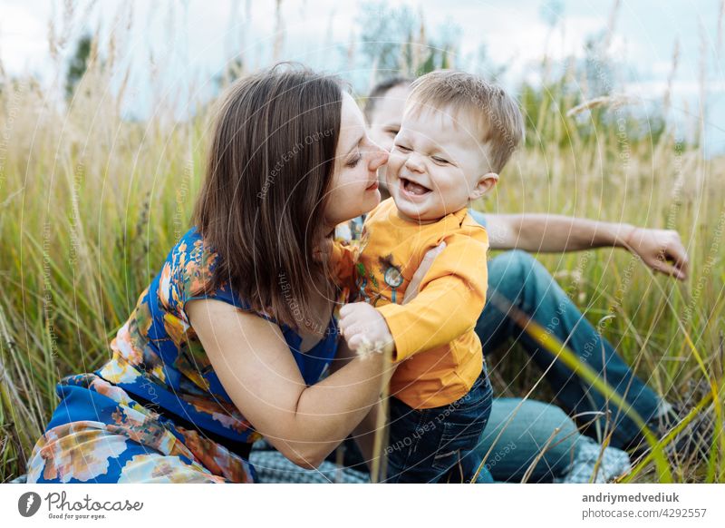 happy family having fun outdoors in grass. Family enjoying life together at meadow. Mother, father, little boy smiling while spending free time outdoors mother