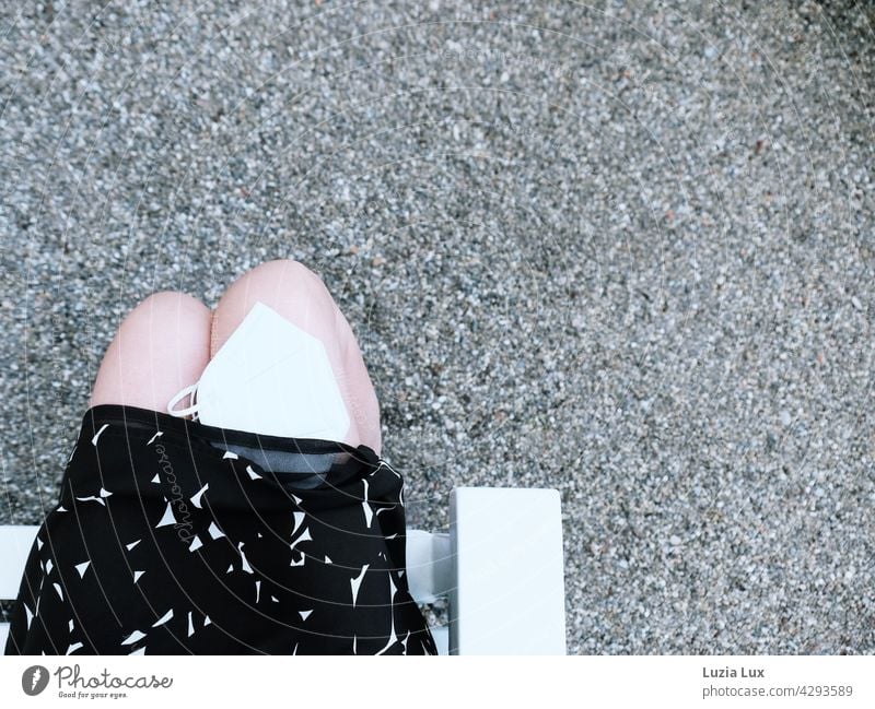 Summer, Corona time: woman in a dress sits in the park, a white mask on her knee has slipped halfway up her skirt Woman with mask Mask Face mask Lifestyle