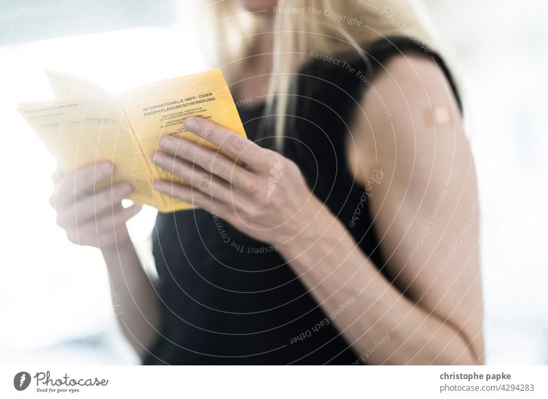 Blonde woman holding vaccination card and has plaster on upper arm after vaccination Woman Immunization Vaccination card corona coronavirus covid-19 pandemic