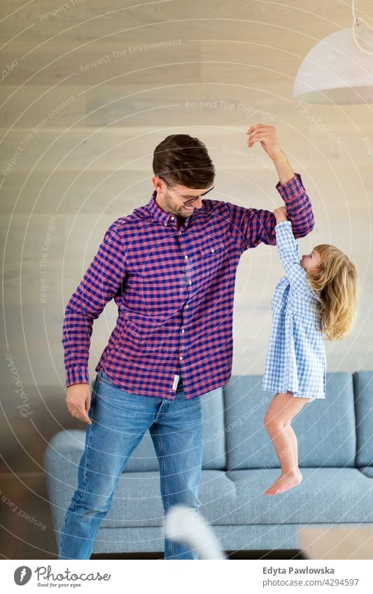 Little girl holding on to her father's arm as he lifts her up home house man dad family parent relatives child daughter little girl kid kids children