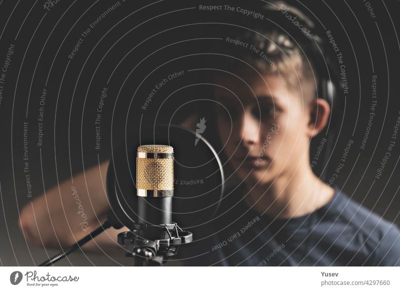 Stylish attractive guy with dreadlocks is recording a song in the studio. A young singer in black studio headphones stands in front of a microphone in the blurred background. Low key lighting.