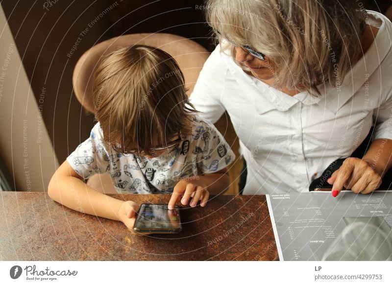 Boy wearing glasses and looking at a display of a mobile under the supervision of an adult Parenting homeschooling surfing the net connection using phone