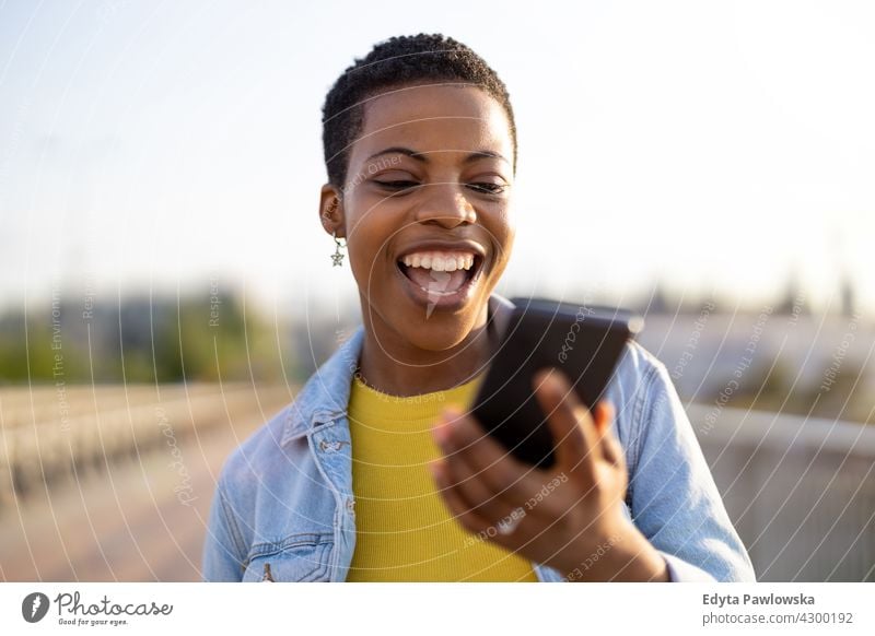 Smiling young woman using smartphone outdoors afro proud real people city life African american afro american student Black ethnicity sunny sunset outside