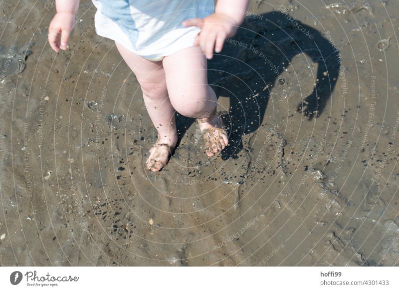 the little child plays and stomps in a puddle in the mudflats Children's Feet Sludgy Slick watt Walk along the tideland slush Dirty Water Wet Puddle North Sea