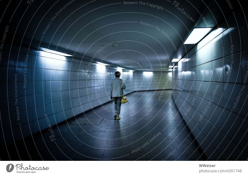 A woman walks alone through the coldly lit passage of a subway station Woman Passer-by Underground Lonely Train station Public Tunnel Walking Going on one's own