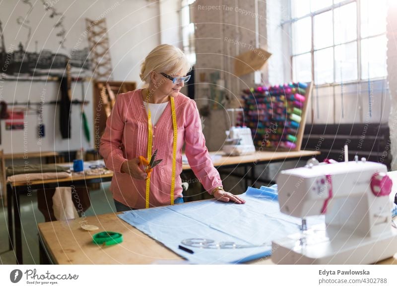 Senior fashion designer  in her workshop Sewing Machine Cloth Fabric Material dressmaker seamstress tailor clothing indoors woman female mechanic owner