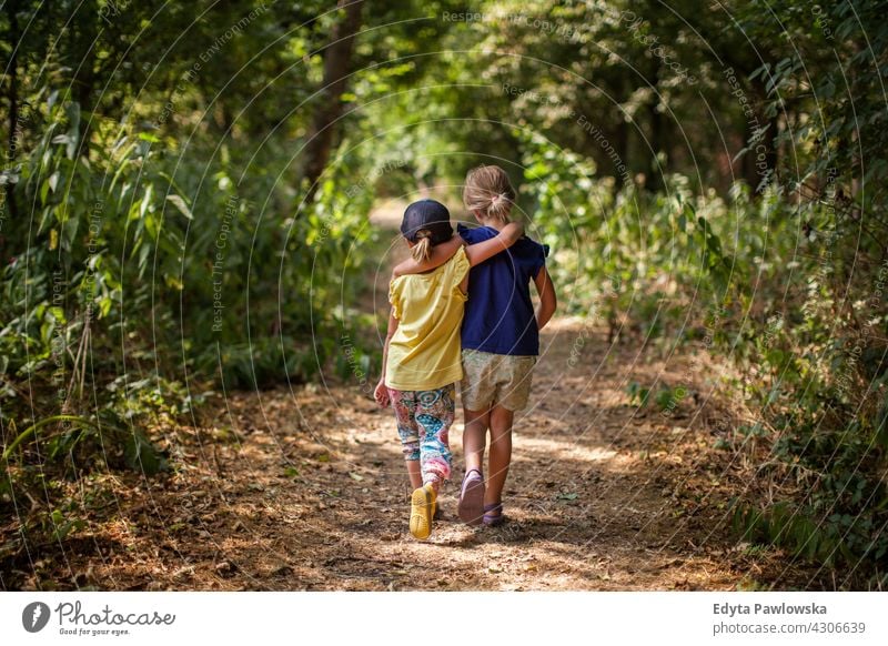 Young children walking in forest friends together hugging sisters summer nature happy outdoor lifestyle sunny activity happiness young leisure girl family