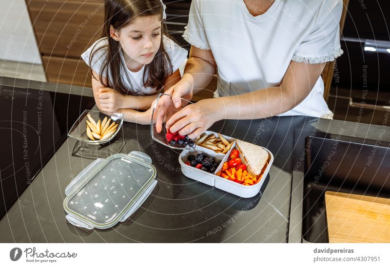 Girl watching her mother putting food in her lunch box fruit organic daughter looking school healthy snack veganism preparing bread sticks placing together