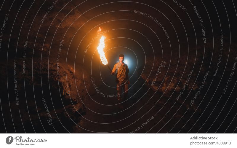 Man with burning fire in dark cave man explore speleology adventure rocky nature geology male torch stone travel tourism subterranean formation rough wild