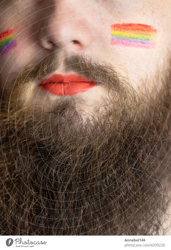 Young handsome bearded man with pride flag on his cheek, rainbow flag standing for LGBTQ, Gender right and sexual minority. Portrait lgbt homosexual equality