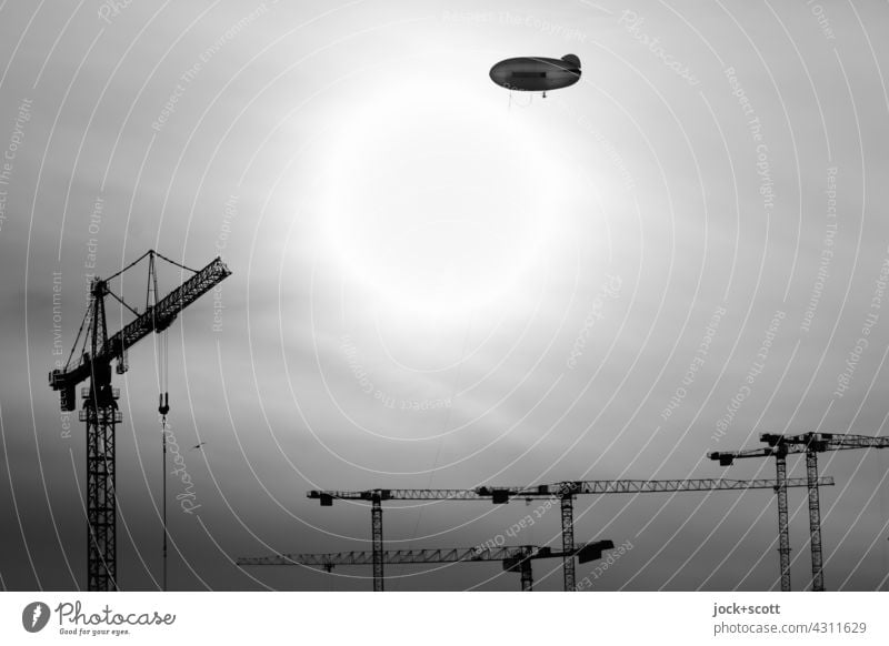 Zeppelin over construction cranes Sun Back-light Sky Construction crane Silhouette Black & white photo Construction site Sunlight Flying price Beautiful weather