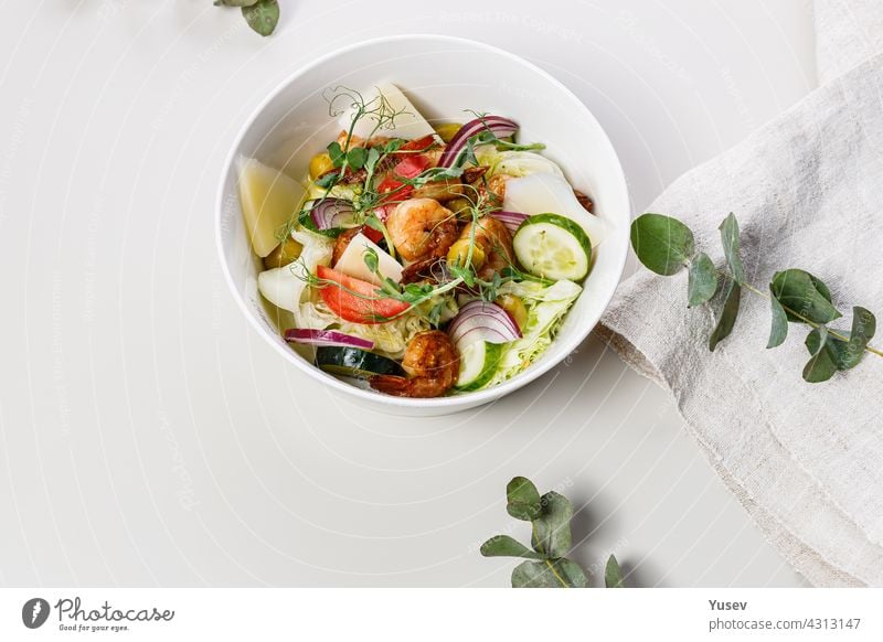 Close-up delicious summer salad with fresh vegetables and seafood on a white background. Seasonal vegetables, shrimp and goat cheese. Healthy Mediterranean natural food. Food photography. Copy space