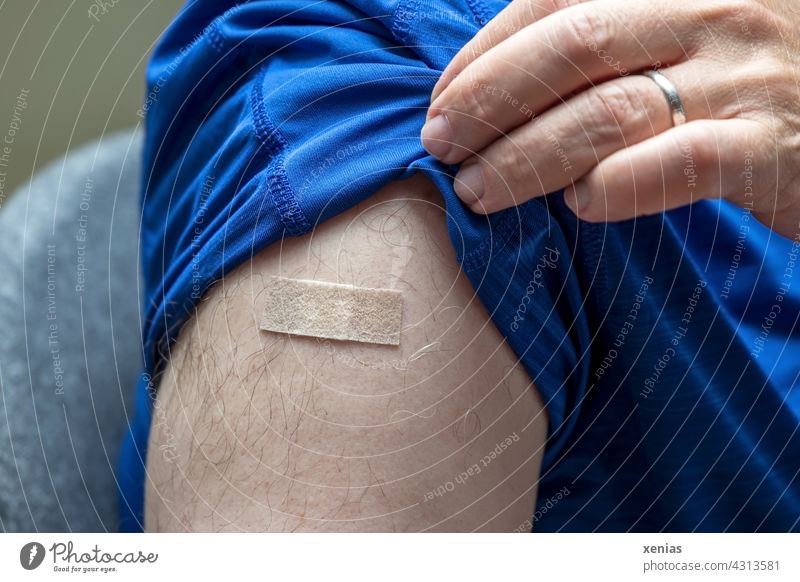 corona thoughts / man in blue t-shirt raises sleeve with fingers to show band-aid after vaccination Immunization pavement Adhesive plaster Man arm Fingers