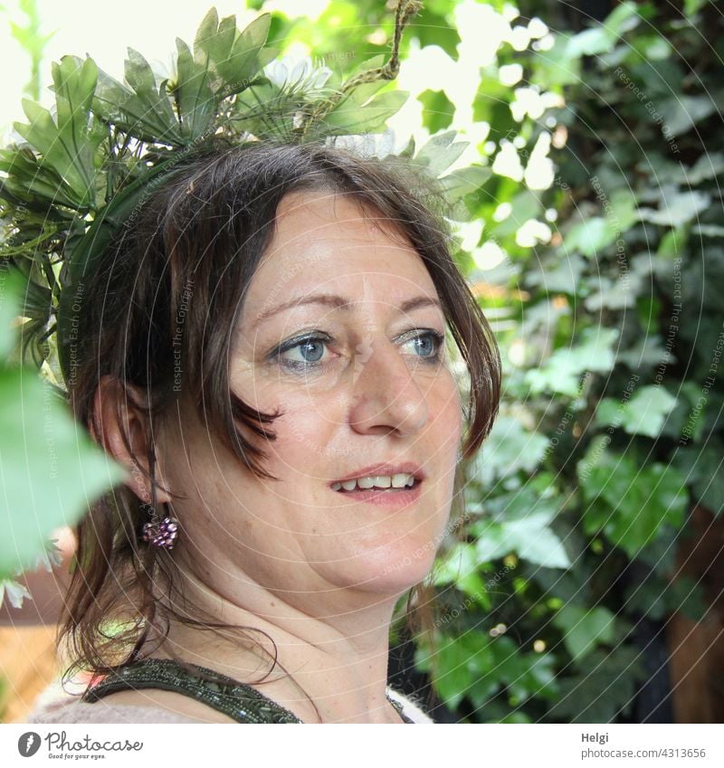 Portrait of smiling woman with brown hair and blue eyes in half profile, in the background are plants portrait Woman feminine Feminine Head Smiling earring Lady