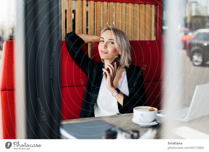 An attractive girl is talking on a mobile phone and smiling, sitting alone in a cafe female tablet businesswoman work coffee happy computer working